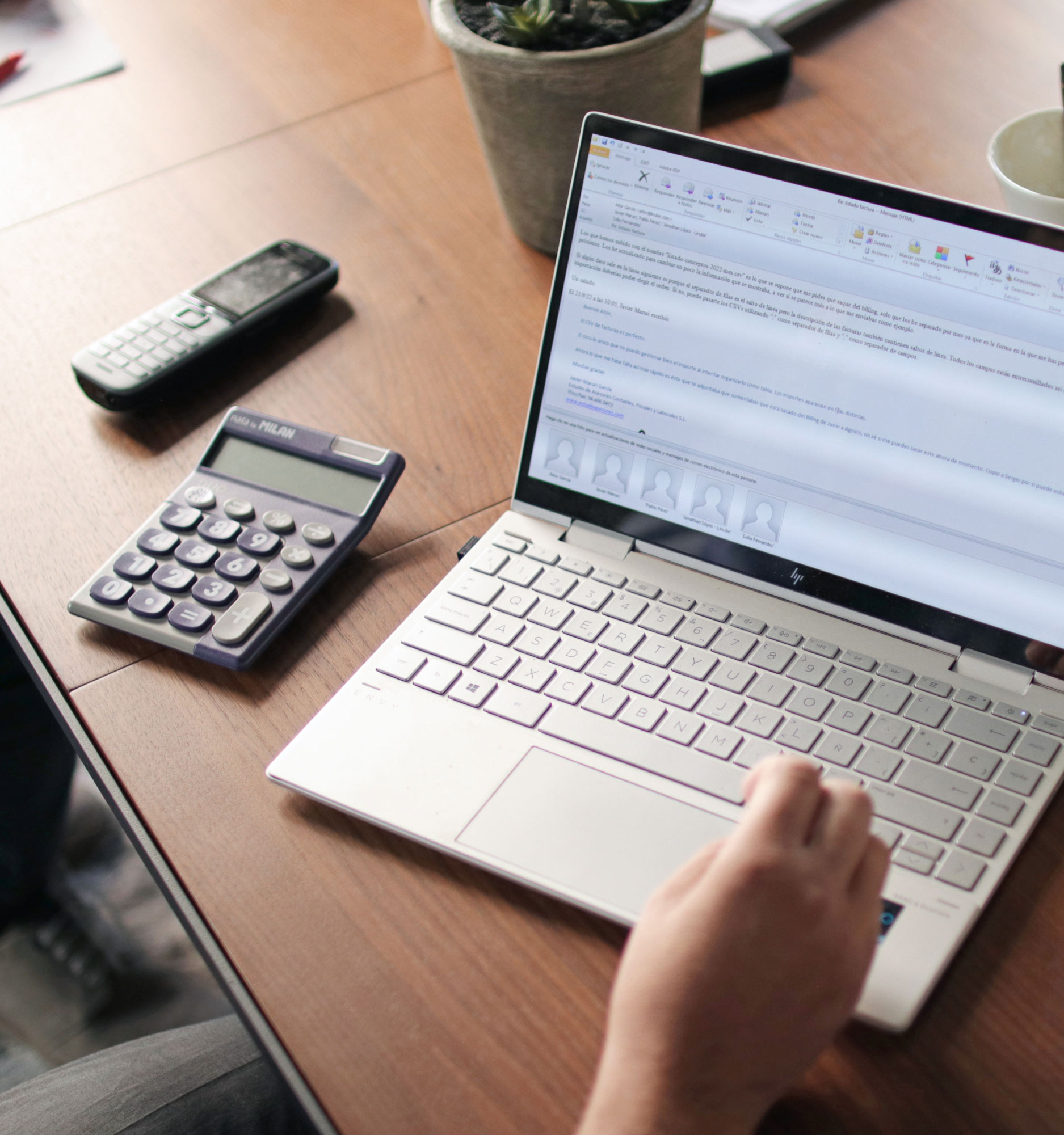 Ordenador portátil sobre el escritorio de oficina y una persona trabajando con él, junto a un teléfono y una calculadora