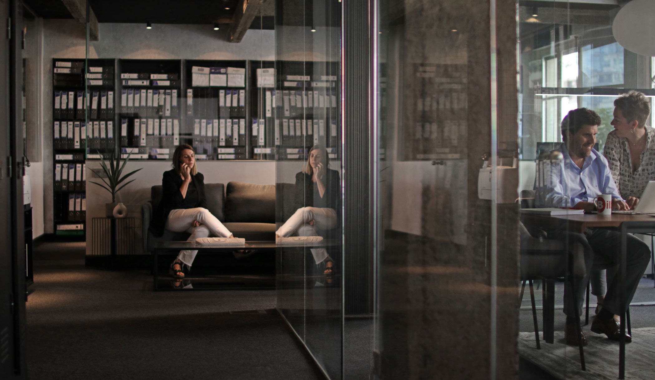 Una persona realiza una llamada de trabajo mientras otras dos personas están reunidas trabajando en la oficina de la asesoría